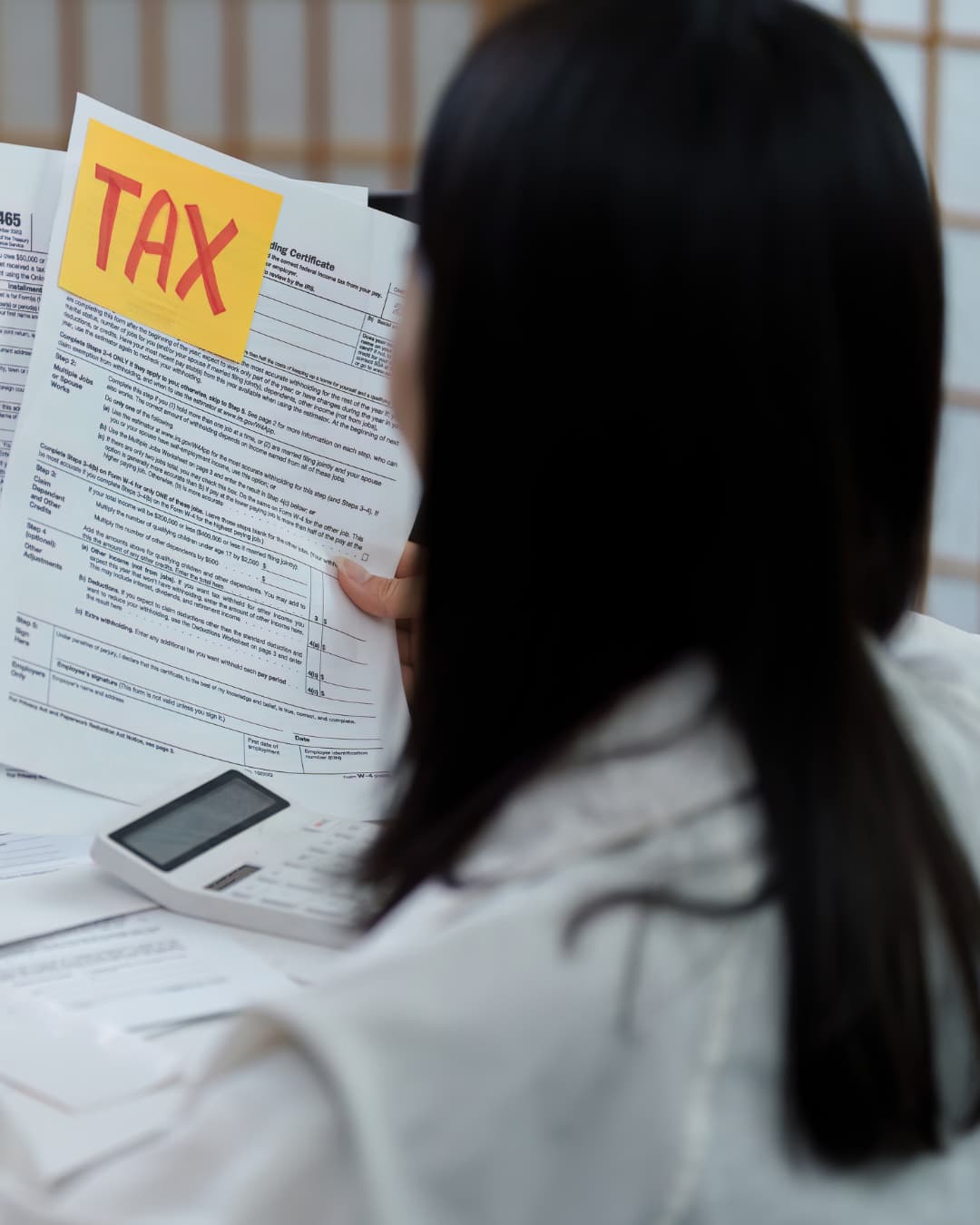 A person reviewing a printed tax form at a desk with a calculator