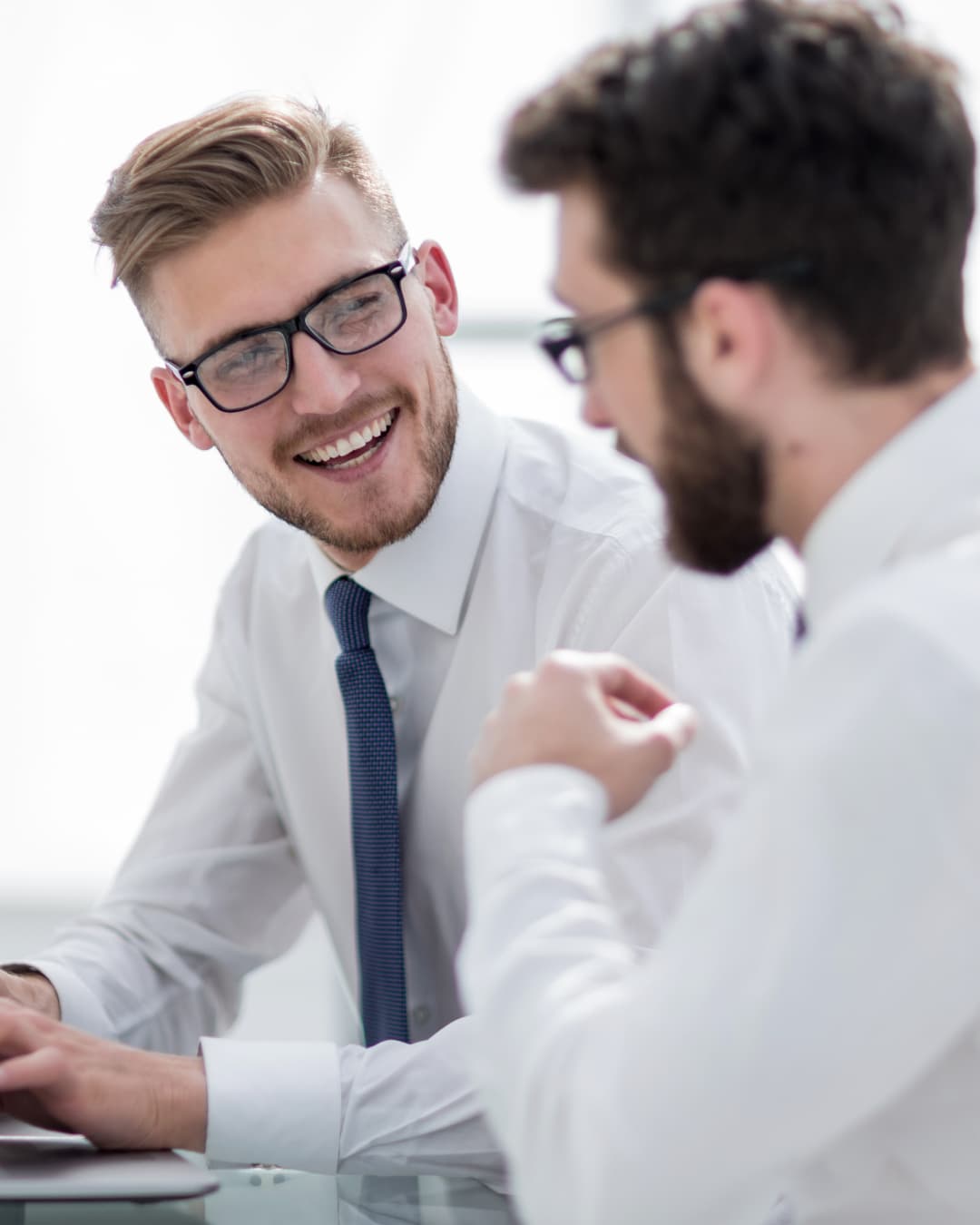 Two colleagues in shirts and ties talking across an office desk
