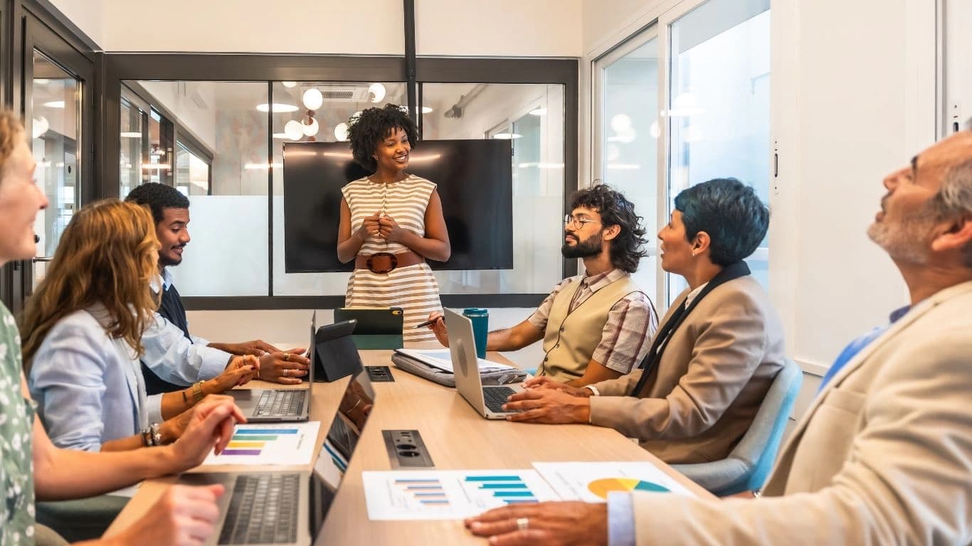 A team meeting with a colleague presenting beside a wall-mounted screen