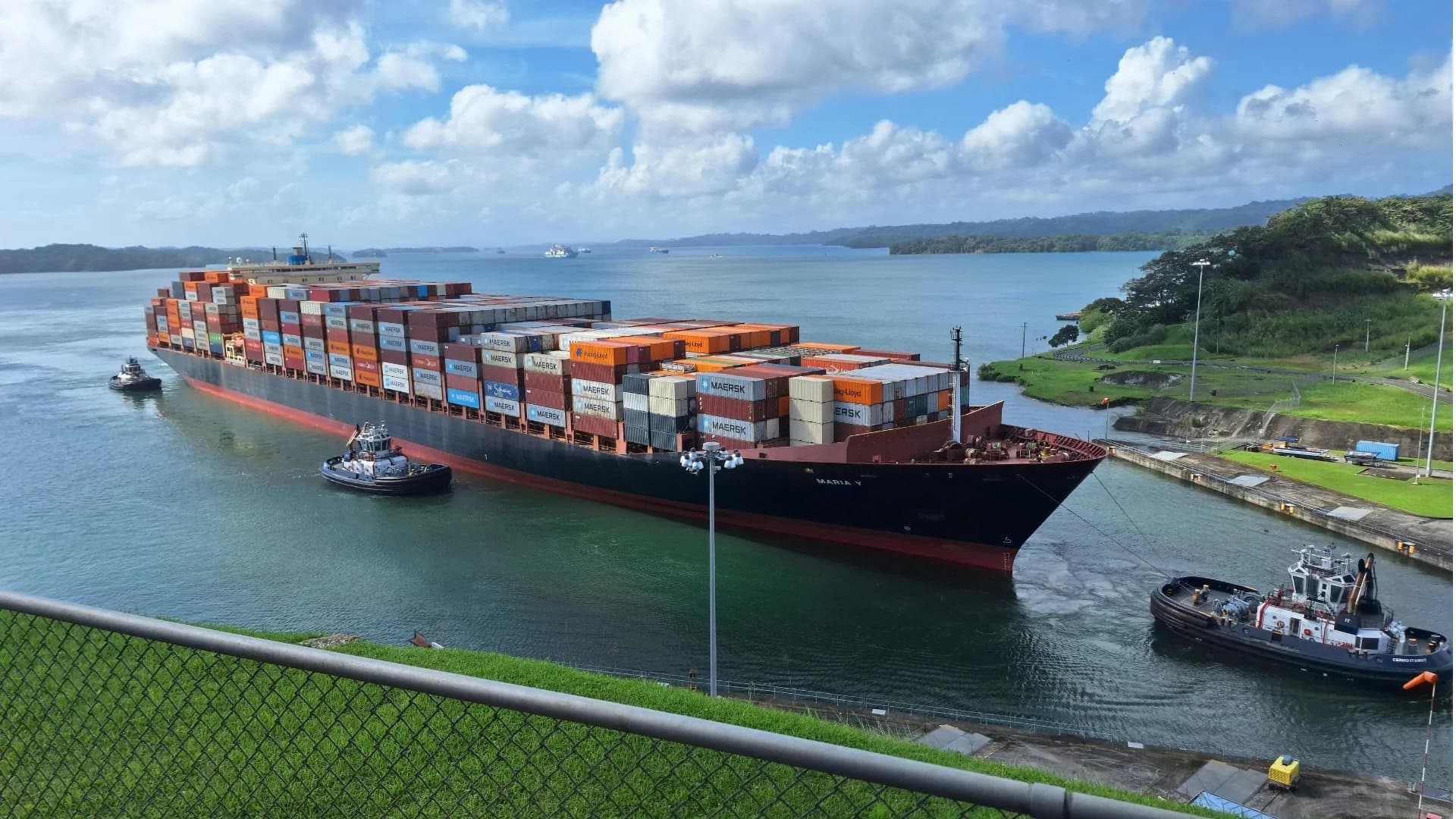 A container ship being guided into port by tugs