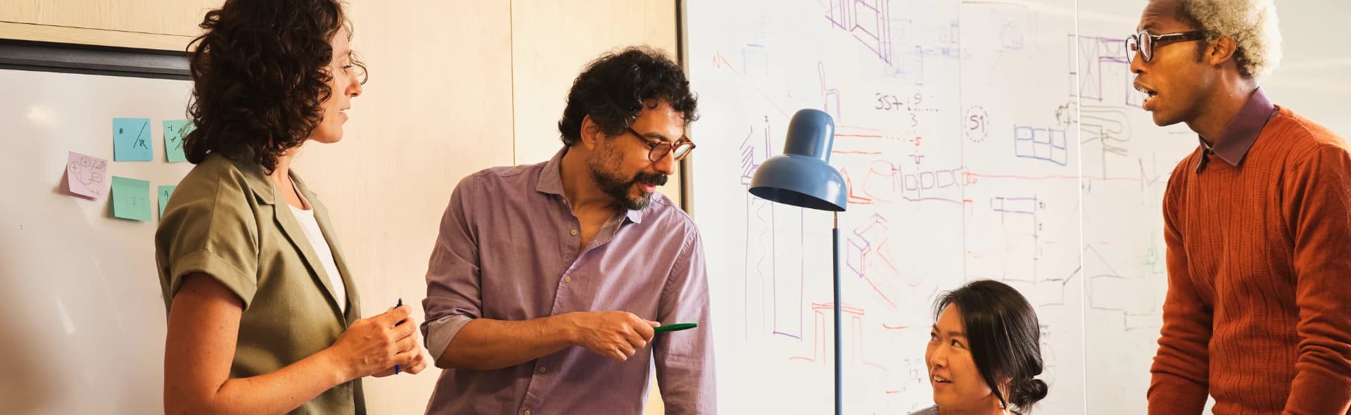 A founder sketching a plan on a glass whiteboard while a colleague watches