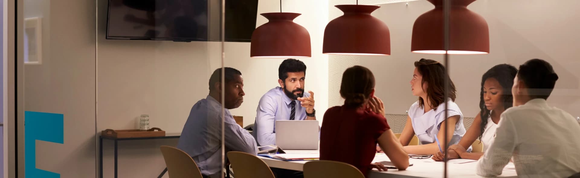 Colleagues talking around a laptop in a glass-walled meeting room